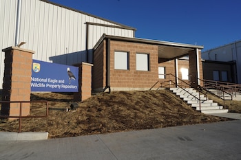 Fachada de un edificio de ladrillo marrón y metal blanco, con un cartel azul que dice 'National Eagle and Wildlife Property Repository' y escaleras con barandillas