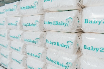 Pila de paquetes de pañales blancos con el logotipo de Baby2Baby y una palmera en azul verdoso, empaquetados en plástico transparente