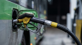 Plano de detalle de una boquilla de surtidor con manguera negra insertada en el tanque de combustible de un autobús verde y gris.