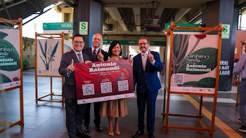 Cuatro personas, sonriendo y señalando, sostienen un cartel rojo de 'Antonio Raimondi', flanqueadas por exhibidores de acuarelas botánicas en una estación de metro