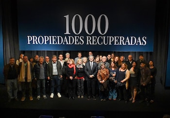 Un grupo de personas de pie en un escenario frente a un fondo oscuro con el texto «1000 PROPIEDADES RECUPERADAS»