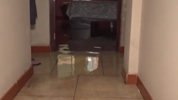 Pasillo interior de una vivienda con el suelo cubierto de agua, con reflejos y una puerta abierta al fondo que da a otra habitación inundada