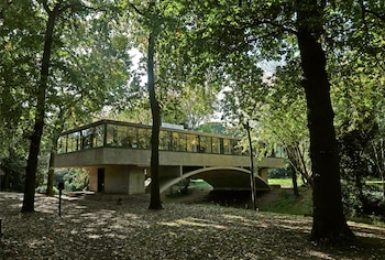 Edificio Museo Casa sobre el Arroyo de hormigón, con grandes ventanales, elevado sobre un arco, rodeado de árboles y hojas caídas en el suelo