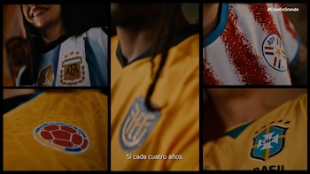 Grupo de futbolistas con camisetas blancas y celestes a rayas se abrazan intensamente en un campo de juego, mostrando unión y emoción