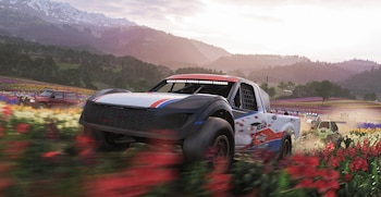 Una camioneta de carreras blanca y azul avanza por un campo de flores coloridas con montañas al fondo