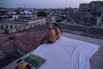 Alexis Mijan y su hijo, Bayron Mijan, están sentados en una cama improvisada en la azotea de un edificio residencial al atardecer en La Habana Vieja, el 11 de agosto de 2026. Muchos cubanos duermen al aire libre durante las noches de verano en busca de alivio ante las altas temperaturas y los frecuentes cortes de electricidad. (Foto de YAMIL LAGE / AFP)