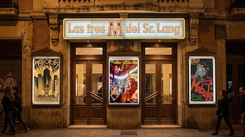 Fachada de cine con marquesina luminosa que dice "Las tres M del Sr. Lang", tres carteles de películas, dos puertas de madera y personas.