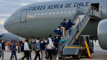 Varias personas y oficiales con chaquetas de la PDI suben por la escalera de abordaje a un avión gris de la Fuerza Aérea de Chile