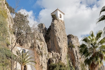 un campanario que sale de la roca y hay más casas entre la mont