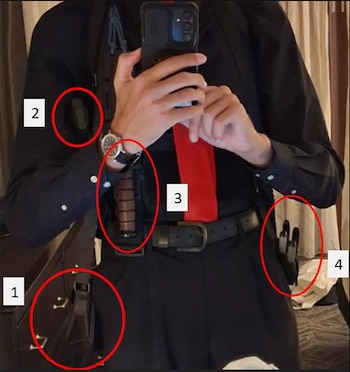 Hombre en camisa negra y corbata roja se toma una selfie en un espejo, mostrando un cuchillo en una funda en la cintura, junto con otras herramientas y un reloj