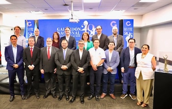 Once personas vestidas con trajes formales posan de pie delante de una pantalla azul con el logotipo del Galardón Nacional a la Exportación