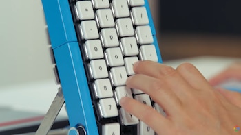 Mano derecha pulsando teclas blancas en un teclado azul dispuesto casi en vertical