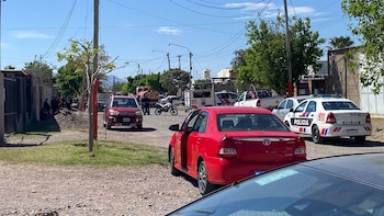 Un automóvil rojo con la puerta abierta se encuentra en una calle de tierra junto a patrullas policiales y un camión de bomberos
