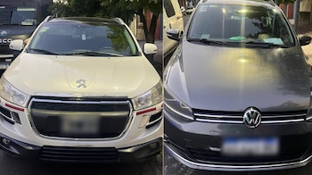 Dos vehículos estacionados en la calle: un SUV blanco de marca Peugeot y un automóvil gris oscuro de marca Volkswagen