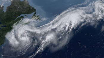 Vista satelital de una gran masa de nubes blancas y grises sobre el océano oscuro, junto a una porción de tierra verde con costas.