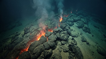 Magma incandescente y rocas oscuras en el fondo marino emiten vapor y burbujas de una dorsal oceánica.