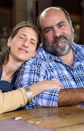 Un hombre con barba y camisa a cuadros azules junto a una mujer que apoya su cabeza en su hombro mientras toma su brazo