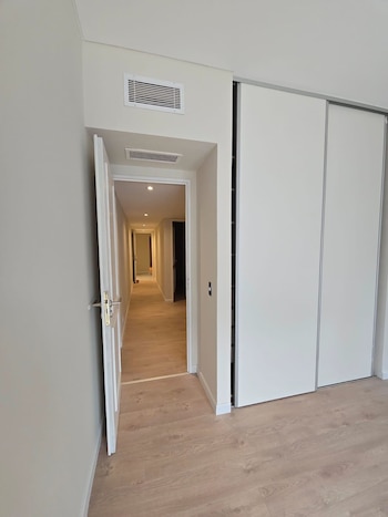 Vista de un pasillo iluminado con luz cálida desde una puerta entreabierta, junto a un armario blanco de puertas corredizas y suelo de madera clara