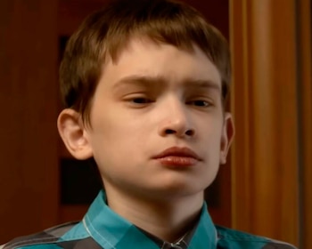 Primer plano de un joven con cabello castaño corto y camisa a cuadros azul y gris, mirando al frente