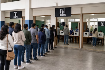 Personas en fila esperan frente a mesas de sufragio con letreros de la ONPE dentro de un recinto escolar.