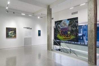 Interior de una galería de arte con paredes blancas, varias pinturas colgadas y un cuadro de gran tamaño suspendido junto a una escalera