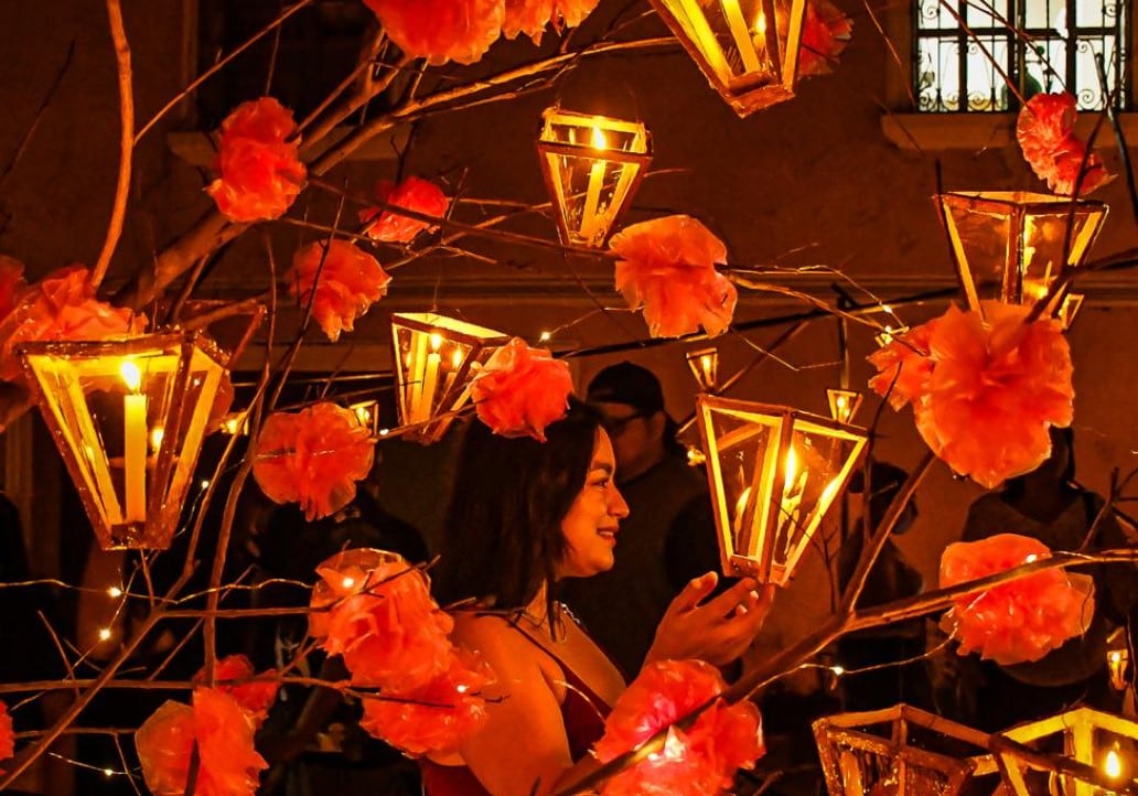 Una visitante observa uno de los faroles artesanales de madera con vela encendida, instalados sobre ramas decoradas en las calles de Ahuachapán (Cortesía: La Noticia SV).