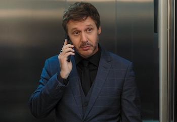 Benjamín Vicuña con barba y pendiente, vestido con un traje azul a cuadros y camisa negra, hablando por un smartphone negro