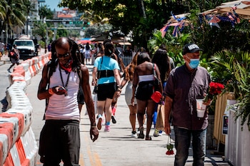 Personas usando tapabocas pasean antes del toque de queda este viernes en el paseo turístico de Ocean Drive en Miami Beach, Florida. EFE/Giorgio Viera