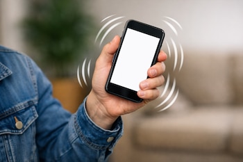 Primer plano de una mano agitando un smartphone negro con la pantalla en blanco, rodeado de ondas blancas que indican movimiento. La persona lleva una chaqueta vaquera.