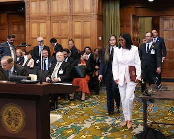Delcy Rodríguez, vestida de blanco, camina en una sala de la CIJ, rodeada de personas, con paredes de madera y alfombra ornamentada