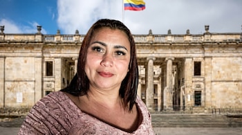 Primer plano de una mujer colombiana con cabello oscuro y blusa de encaje rosa, sonriendo ante la fachada neoclásica del Capitolio Nacional de Colombia y la bandera.