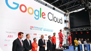 Hombres en traje y pilotos con monos deportivos están en un escenario ante una gran pantalla con el logotipo de Google Cloud y Fórmula E