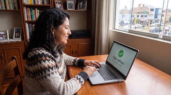 Mujer sentada frente a una computadora portátil, tecleando. La pantalla muestra el mensaje "Pago exitoso" con un icono de verificación verde.