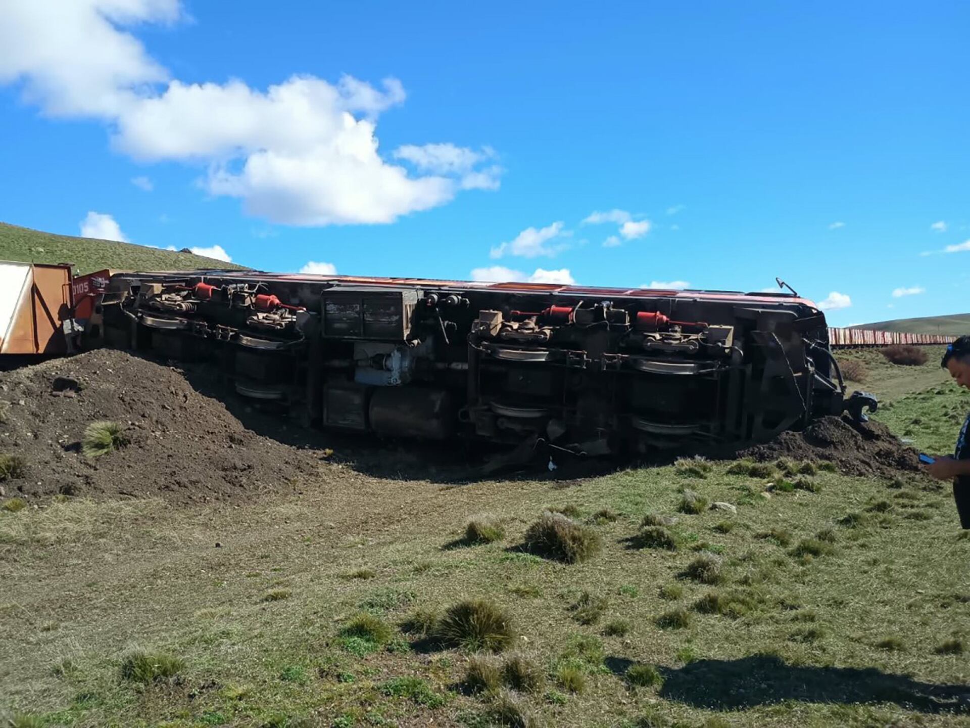 Un vagón de tren yace volcado sobre un terraplén en una zona rural tras sufrir un descarrilamiento.