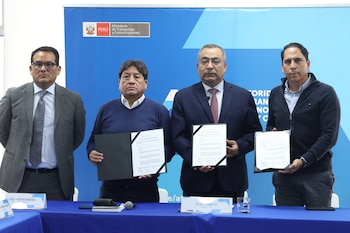 Cuatro hombres de pie sostienen documentos firmados en una sala. El fondo muestra el logo del Ministerio de Transportes y Comunicaciones de Perú