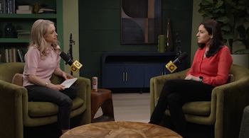 Dos mujeres sentadas en sillones de terciopelo verde conversan frente a micrófonos en un estudio. Se ve una mesa, una lata de café y estantes al fondo