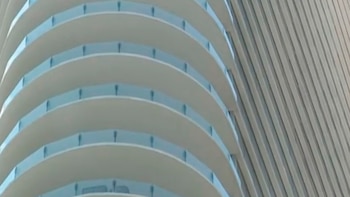 Fachada de un rascacielos mostrando una serie de balcones curvos blancos con barandillas azules y una pared lateral con paneles verticales paralelos