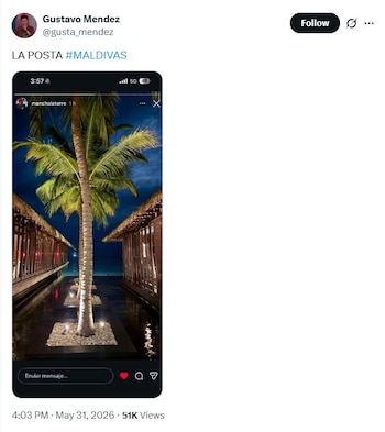Imagen nocturna de un resort en Maldivas: palmera tropical central, camino de agua con luz y bungalows de techo de paja a ambos lados bajo un cielo oscuro
