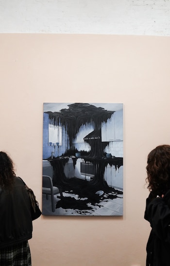 Una pintura colgada en una pared muestra una cocina cubierta por un líquido negro, mientras dos personas la observan de espaldas