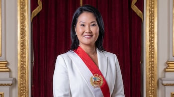 Retrato de Keiko Fujimori, mujer con cabello oscuro y traje blanco, luce una banda presidencial de Perú con su escudo, frente a un telón rojo y marcos dorados.