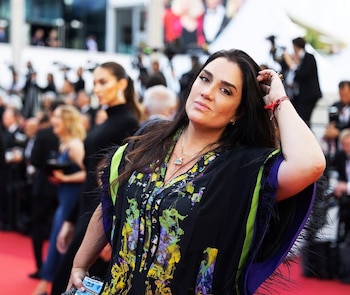 Lucero Boza, con cabello oscuro suelto y vestida con un kaftán estampado floral, posa en una alfombra roja con gente borrosa detrás