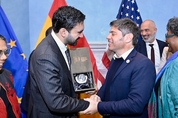 Axel Kicillof entrega una caja con un mate a un hombre, frente a las banderas de la Unión Europea, España y Estados Unidos