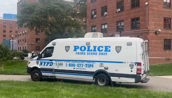 Una camioneta blanca de la policía con la inscripción Crime Scene Unit está estacionada junto a edificios de ladrillo rojo