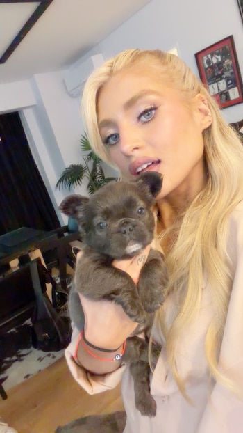 Una mujer con cabello rubio sostiene un pequeño cachorro gris oscuro con ambas manos