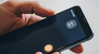 Primerísimo plano de una mano sosteniendo un smartphone negro, con el icono de NFC claramente visible en la esquina superior derecha de la pantalla.