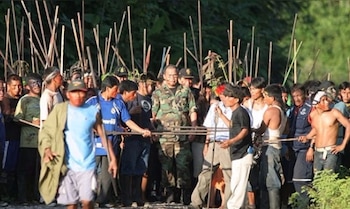 Un grupo numeroso de hombres indígenas, algunos con lanzas y pintura facial, rodea a un oficial con uniforme camuflado en un entorno selvático