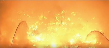 Chorros de agua dirigidos hacia una zona en llamas cubierta por fuego y humo anaranjado