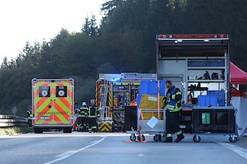 Una ambulancia y un camión de bomberos estacionados en una carretera mientras los servicios de emergencia despliegan su equipo