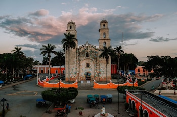 Iglesia de piedra con dos torres y decoración colorida en la fachada. Palmeras, edificios, mototaxis, personas y cielo nublado