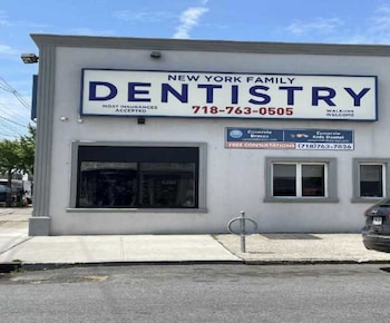 Fachada de un edificio blanco con un letrero azul New York Family Dentistry. Letreros Canarsie Braces y Kids Dental. Ventanas, acera y coche negro